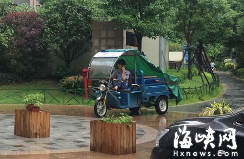 這名快遞哥騎行在小區(qū)通道內(nèi)，一邊接打手機(jī)，一邊還把腳架在車前欄桿上